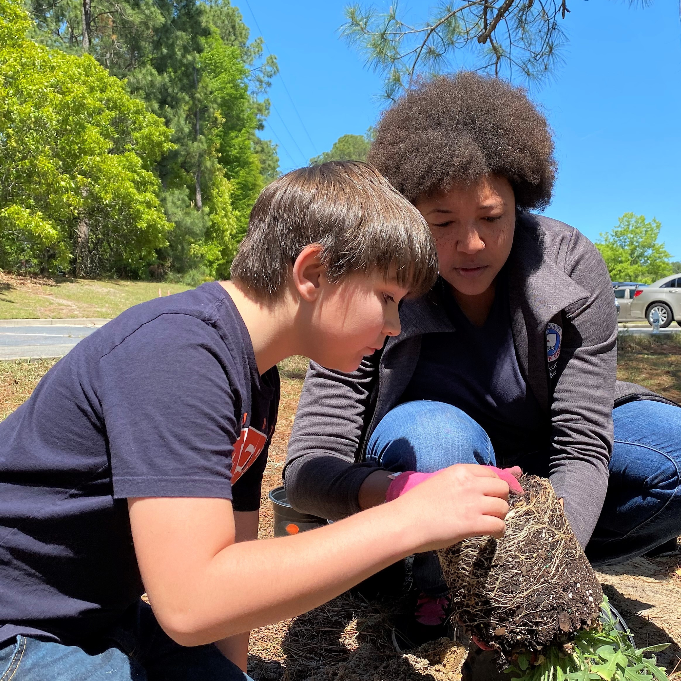 Educator shows root system of a potted plant to child.