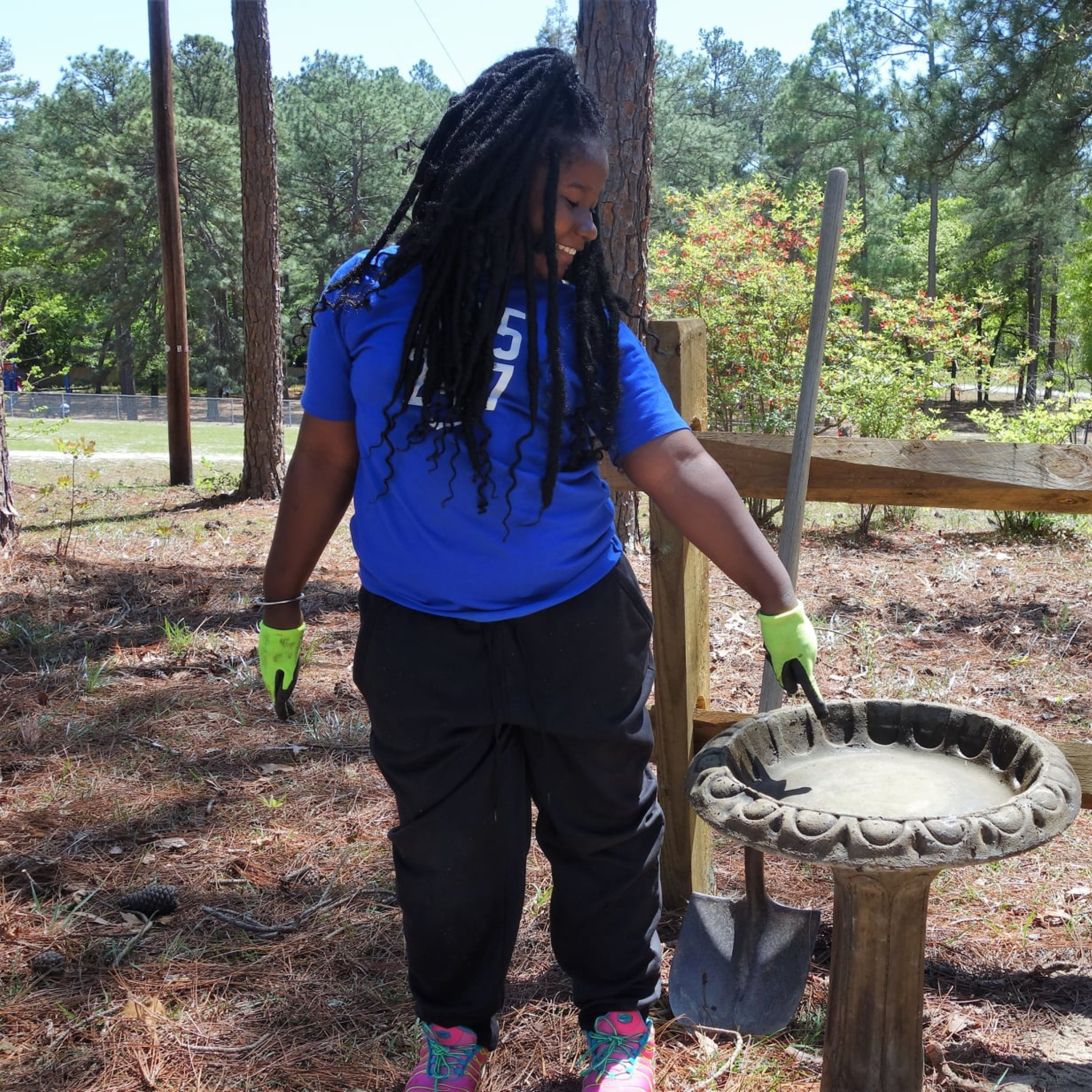 GSS_4 Young girl wearing work gloves, having worked in a school garden -- points to a bird bath.